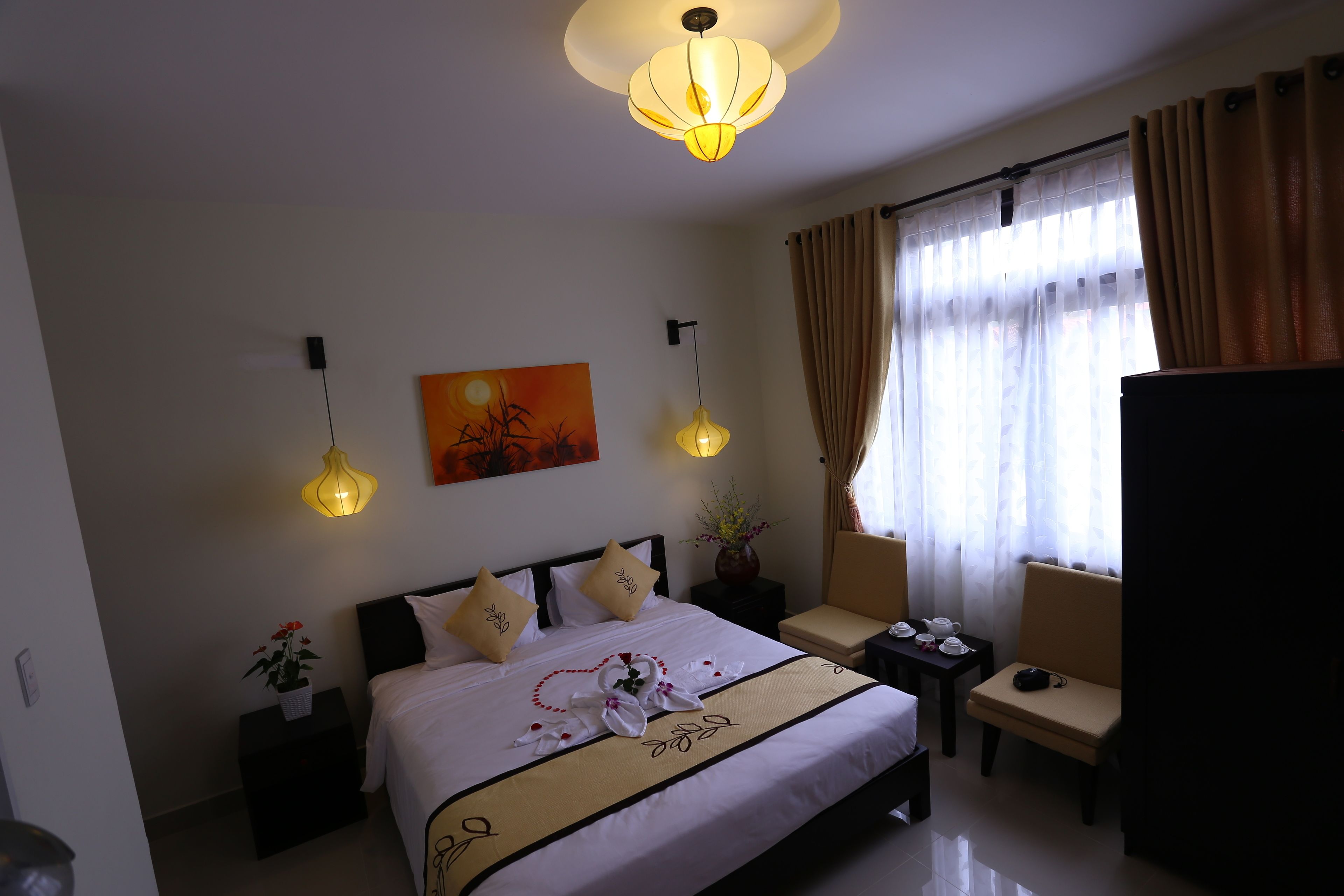 A hotel room with a bed, bedside table, chair, and a painting on the wall.