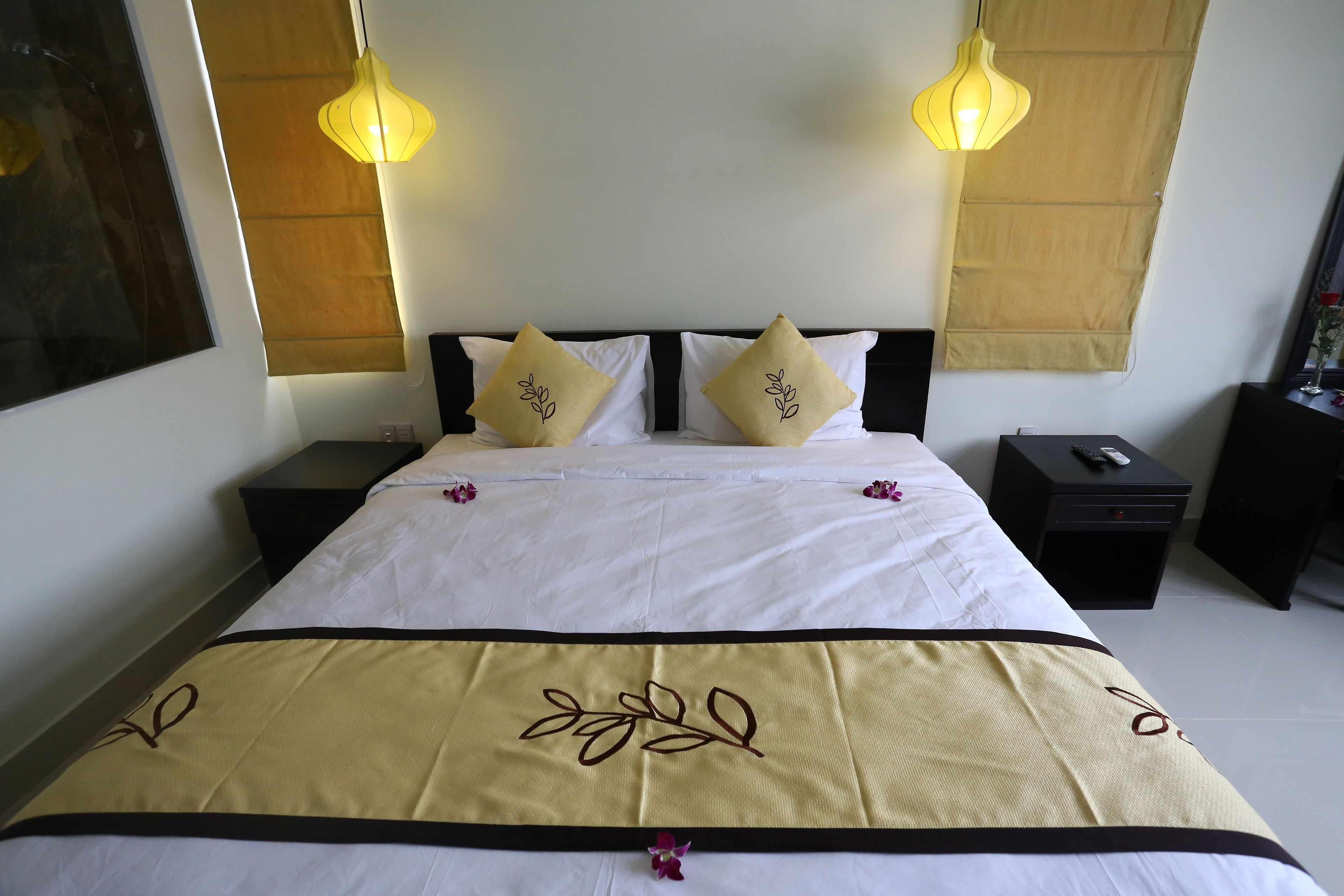 A neatly made bed with white and beige bedding, two bedside lamps, and a nightstand with a remote control.