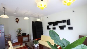 A modern living room with a sofa, a dining table, and a coffee table. There are two pendant lights, a clock, and a plant. - Hoi An Cottage Villa (Da Nang)