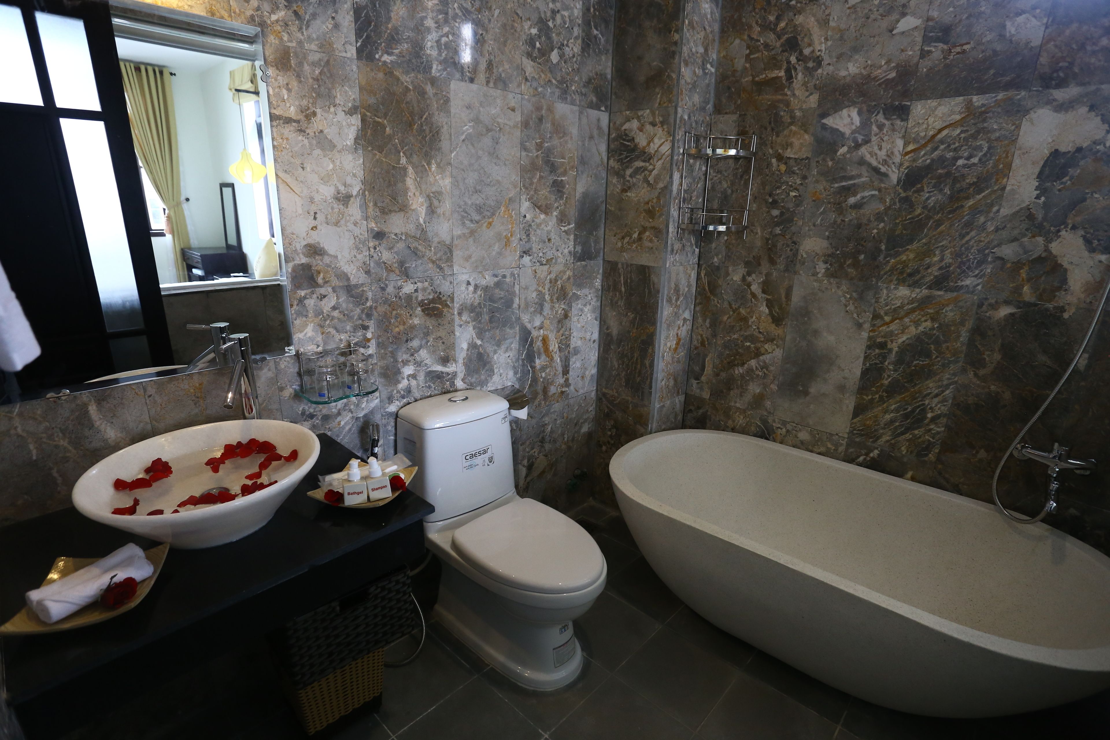 Un baño con pared de mármol, un lavabo blanco, un inodoro y una bañera.