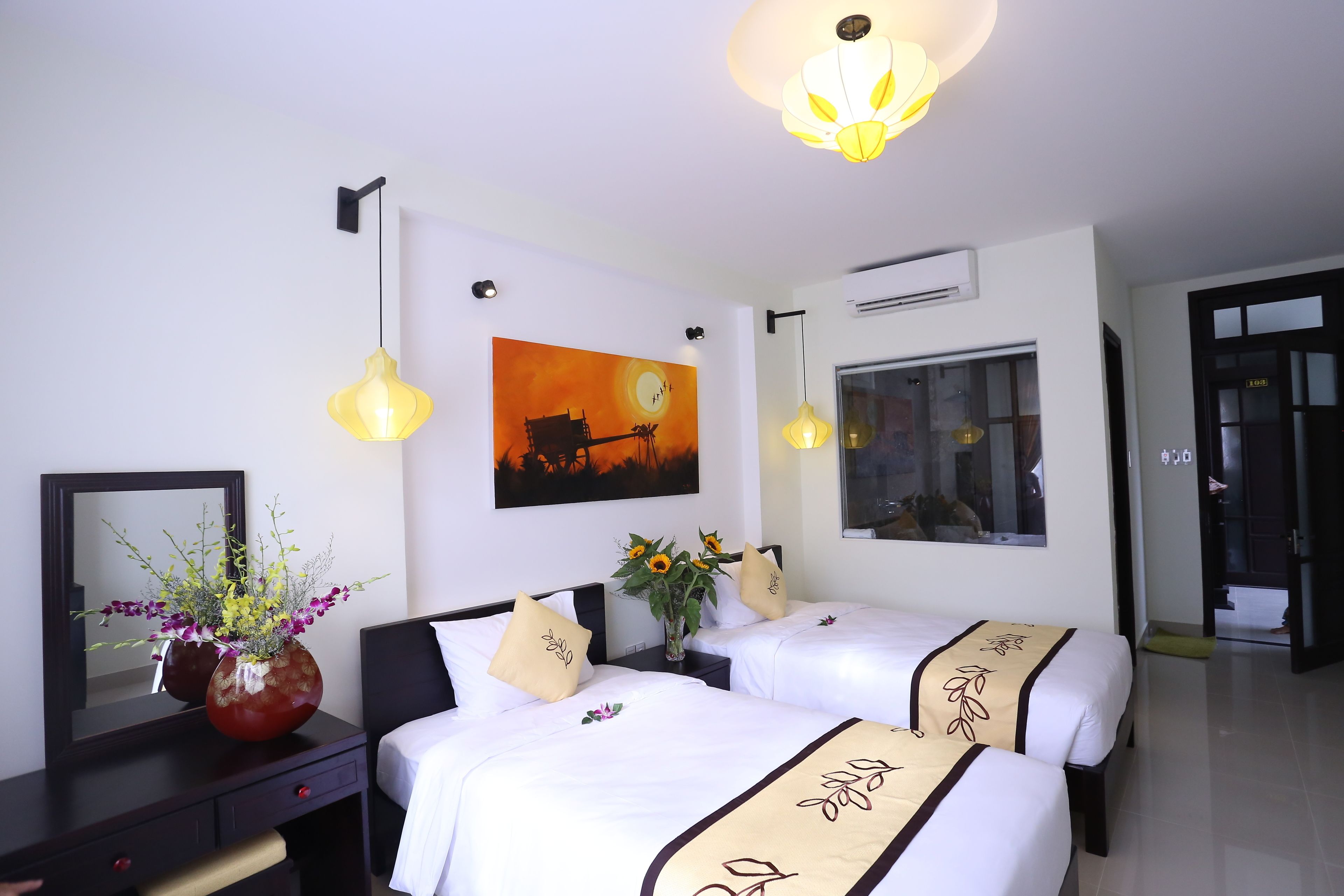 A hotel room with two beds, a large mirror, a painting, and a vase with flowers.
