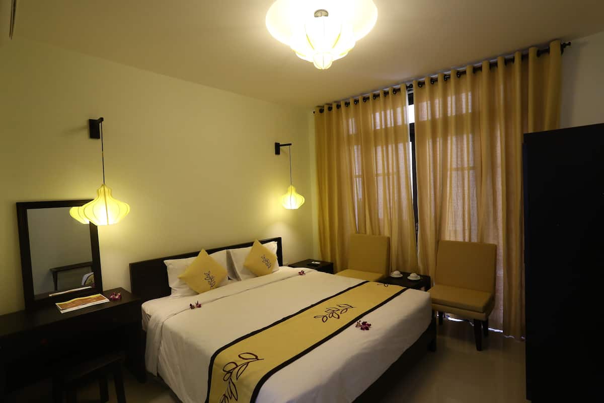 Ein Hotelzimmer mit einem Bett, Nachttischen, einem Sessel, einem Schreibtisch, einem Spiegel und einer Chandelier.