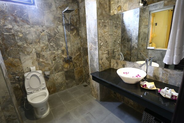 A bathroom with a marble wall, a toilet, a sink, and a shower.