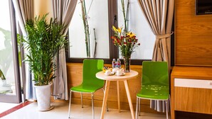 Una camera d'albergo con due poltrone verdi, un tavolino rotondo con un vaso di fiori e una pianta in vaso.