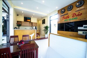 A modern kitchen with wooden cabinets, a dining area with a glass table and wooden chairs, and a wall with clocks and a sign for 'Bien Dao Sea Island'. - Bien Dao Homestay Hoi An (Da Nang)