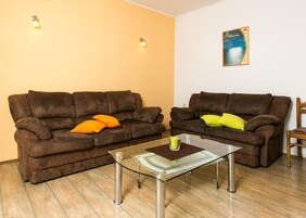 A living room with two brown sofas, a glass coffee table, and a small table with a glass of juice.
