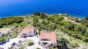 Una propiedad costera con dos edificios, un camino de entrada pavimentado y vista al mar.