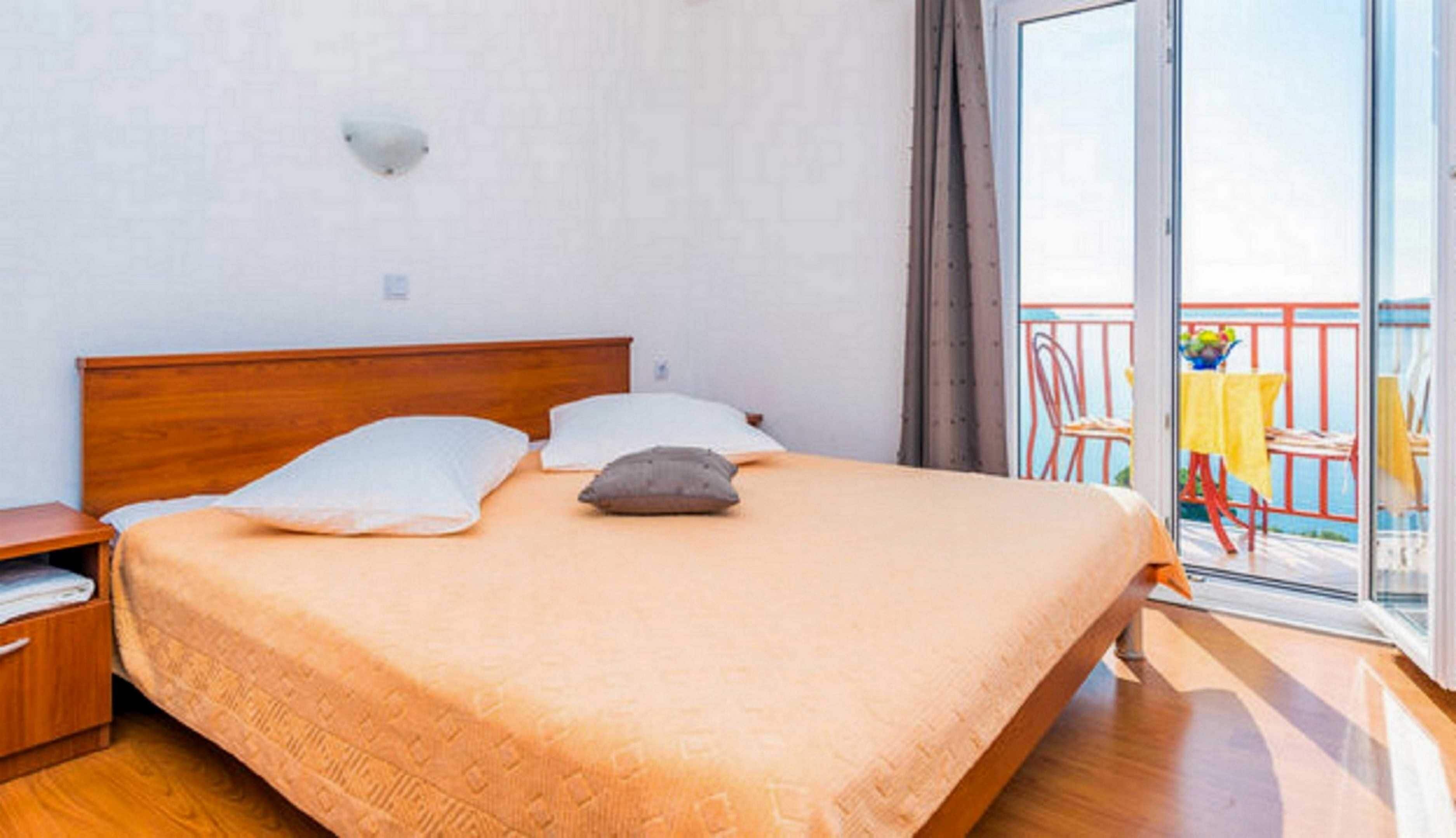 A bedroom with a wooden bed, two pillows, a nightstand, and a balcony with a table and chairs.