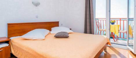 A bedroom with a wooden bed, two pillows, a nightstand, and a balcony with a table and chairs.