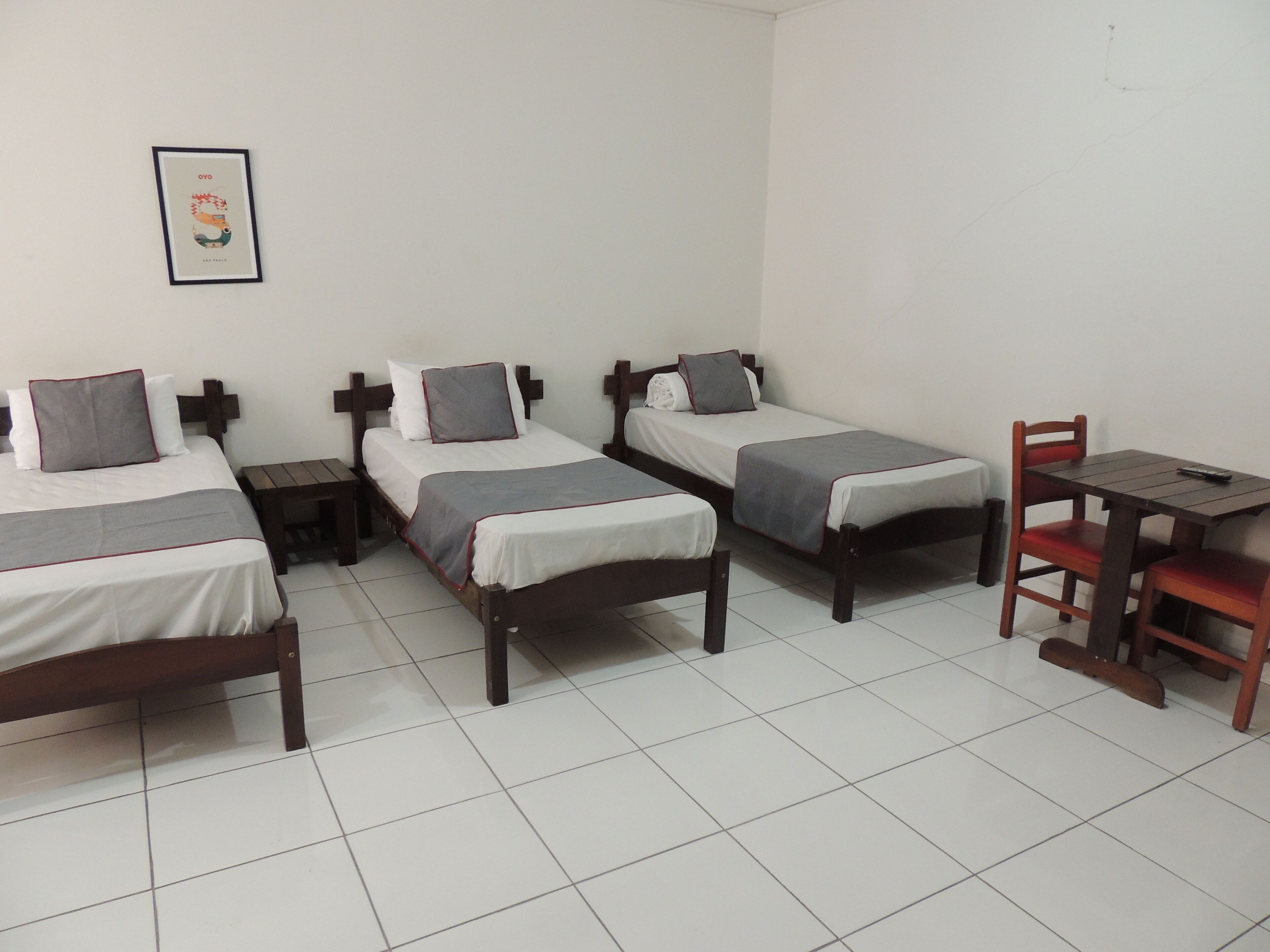A room with three single beds, a small table, and a chair.