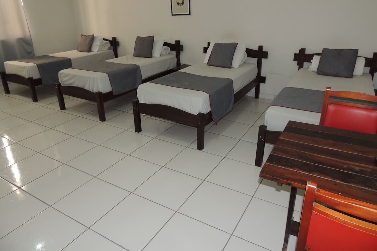 A hotel room with four single beds, each with a pillow and a blanket. There is a wooden table and a red chair in the room.