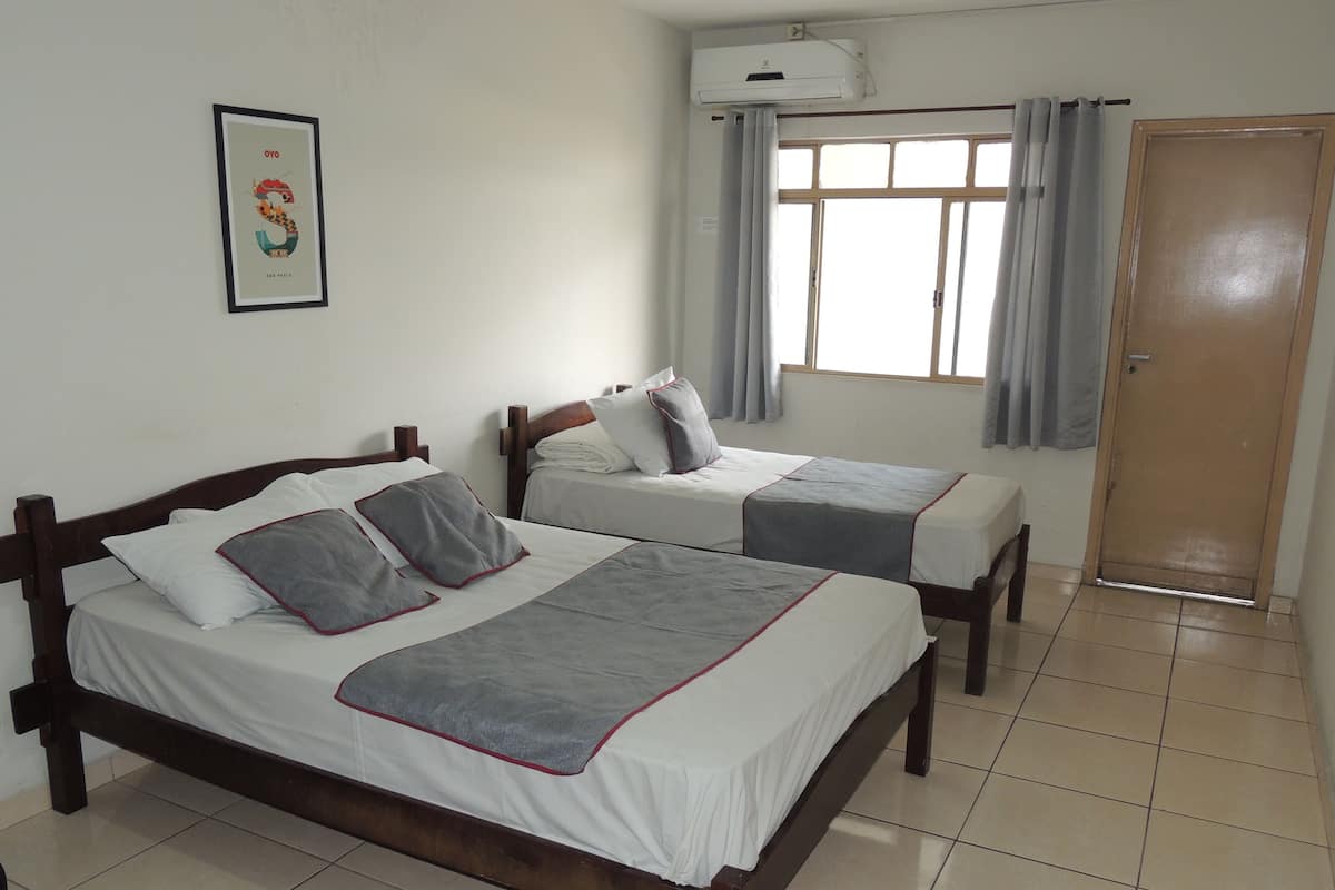 A hotel room with two wooden beds, a window with curtains, a door, and a framed picture on the wall.