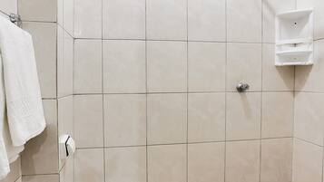 Casa de banho pequena e revestida a azulejos, com sanita, chuveiro e suporte para toalhas.