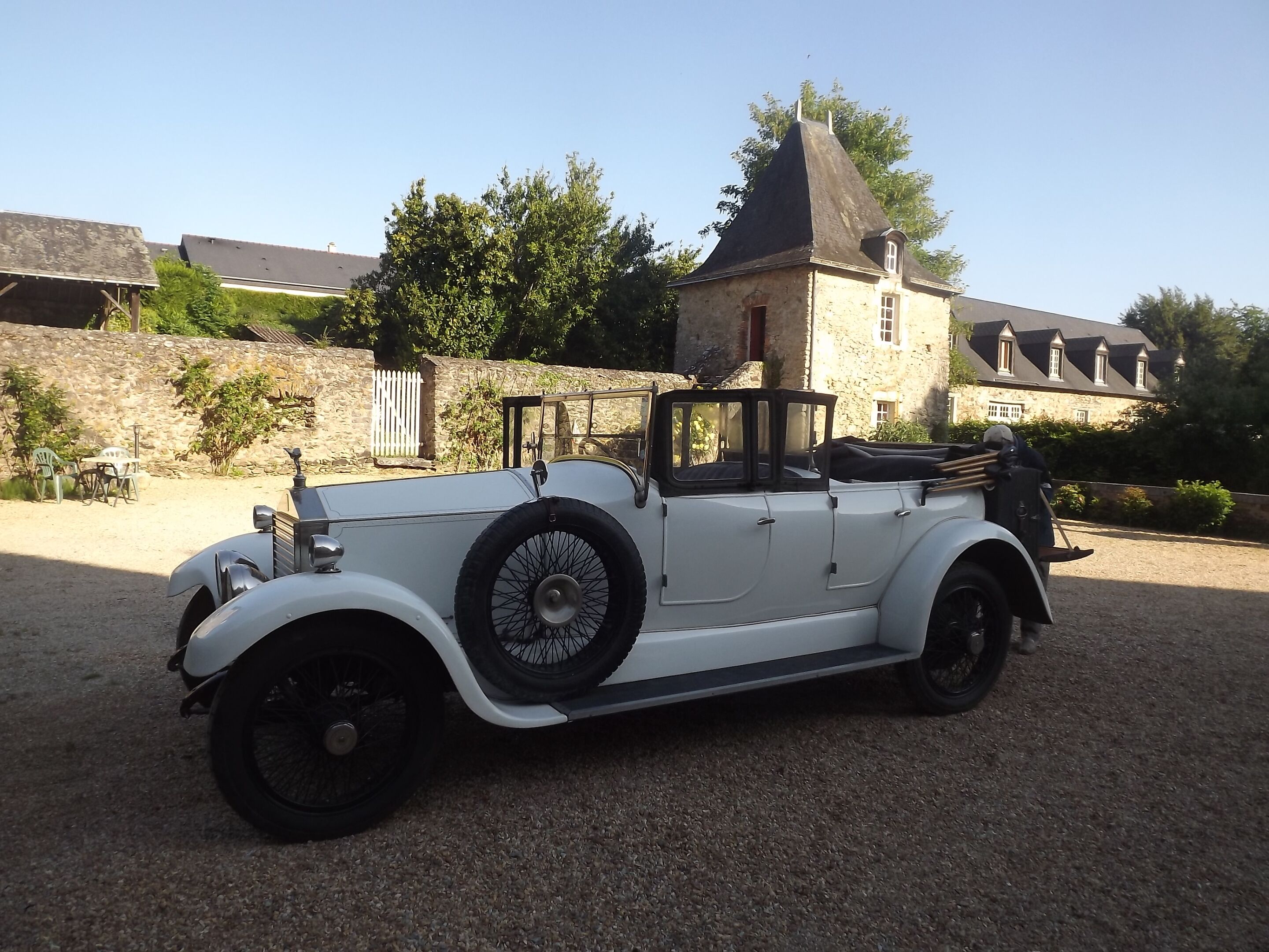 A vintage white convertible car parked on a gravel surface.