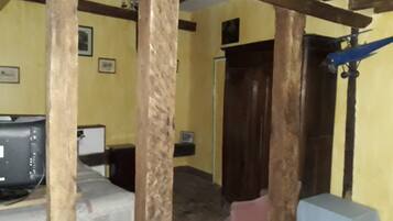 A room with a wooden ceiling, a television, a small table, and a door.