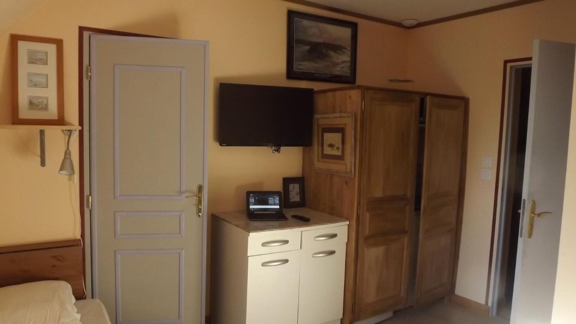 A bedroom with a bed, a desk with a laptop, a wardrobe, a television, and a door.