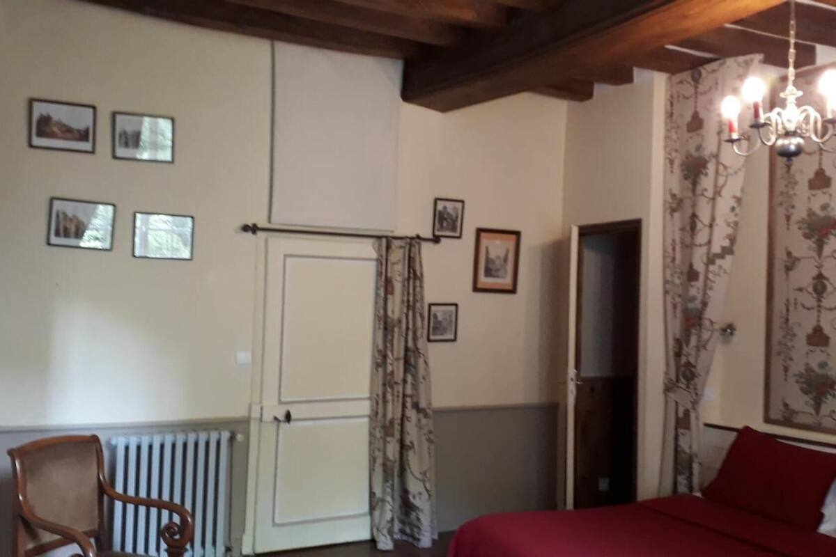A bedroom with a bed, a chair, a radiator, a door, and a chandelier.