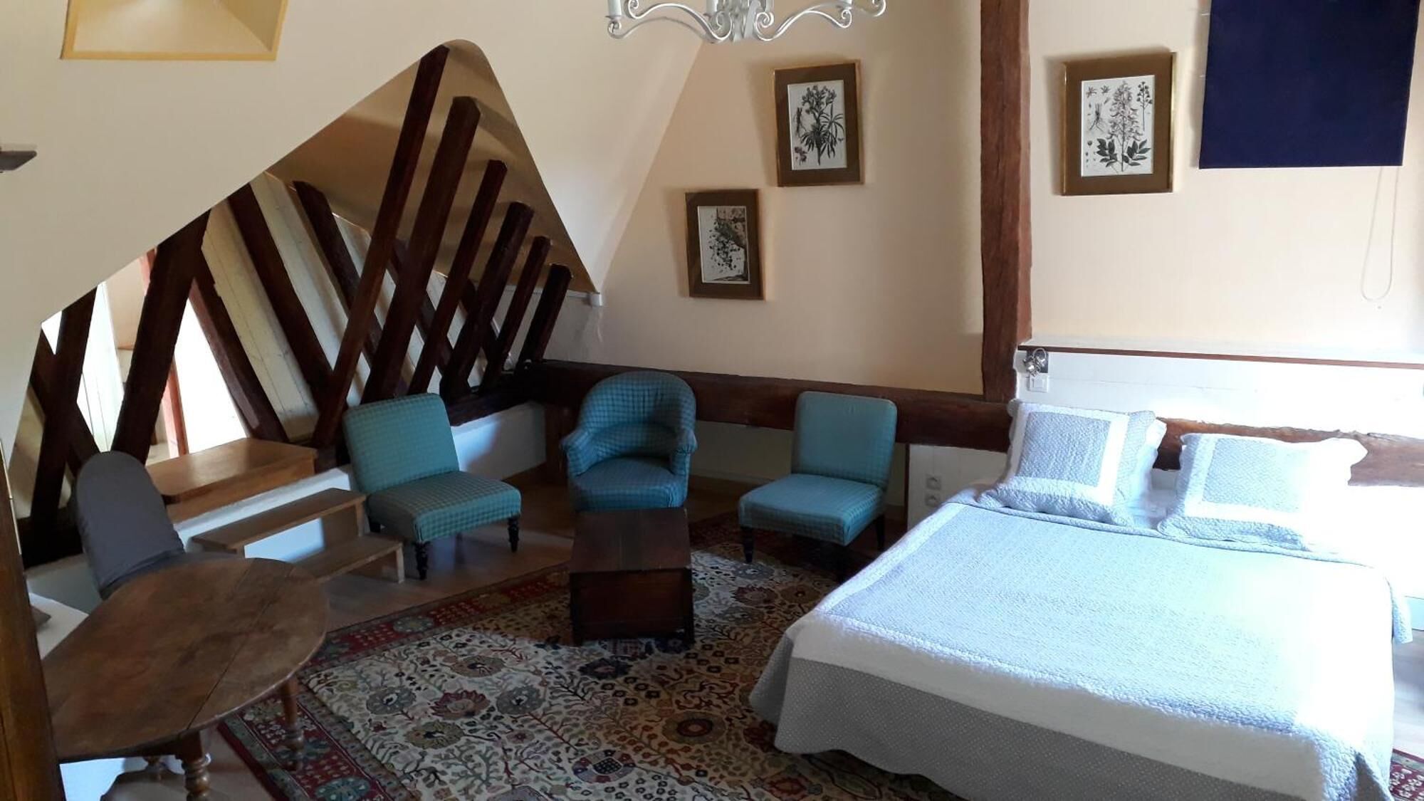 Een slaapkamer met een bed, twee fauteuils, een tafeltje en een kamerkleed met een patroon.