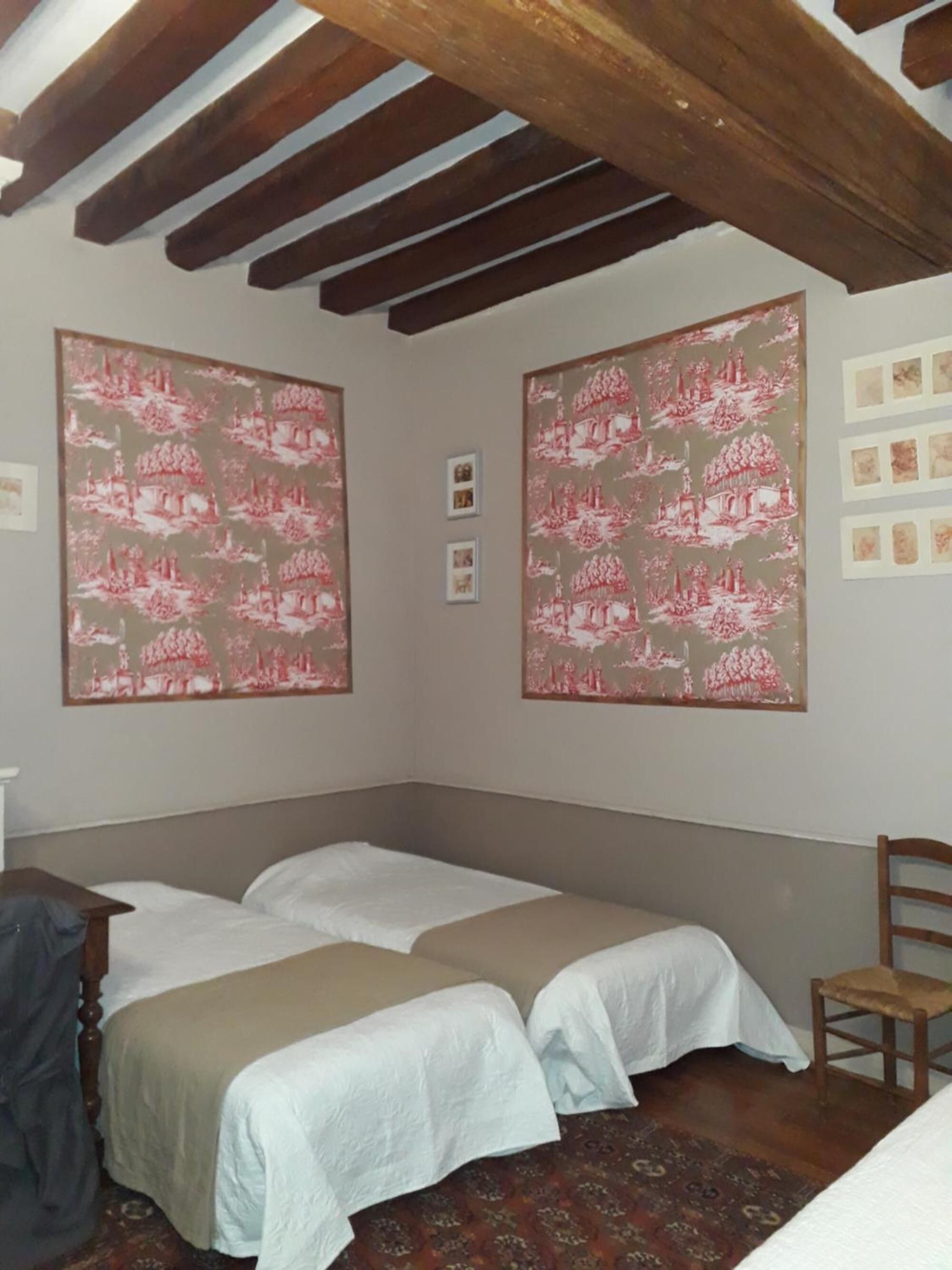 A room with two beds, wooden beams on the ceiling, and large patterned wall art.