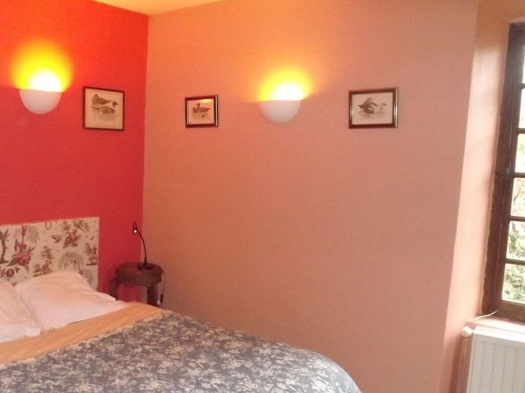 A bedroom with a bed, a nightstand, wall-mounted lights, and framed pictures.