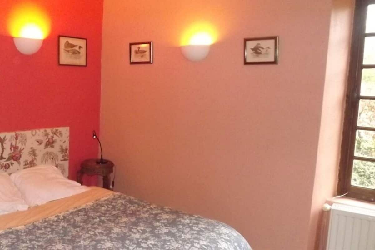 A bedroom with a bed, a nightstand, wall-mounted lights, and framed pictures.
