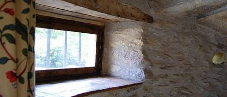 A stone-walled room with a small window and a wooden beam ceiling.