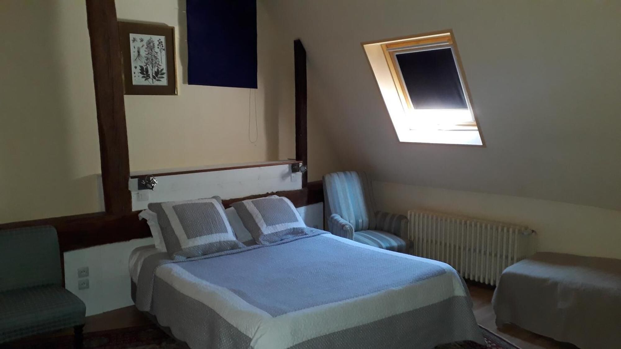 Un dormitorio con cama, una silla, un radiador y un ventanal pequeño.