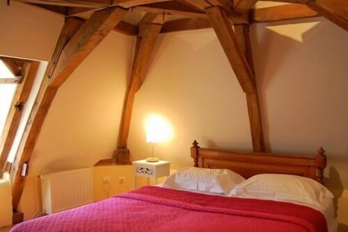 A bedroom with a wooden ceiling, a bed with white bedding, and a nightstand with a lamp.