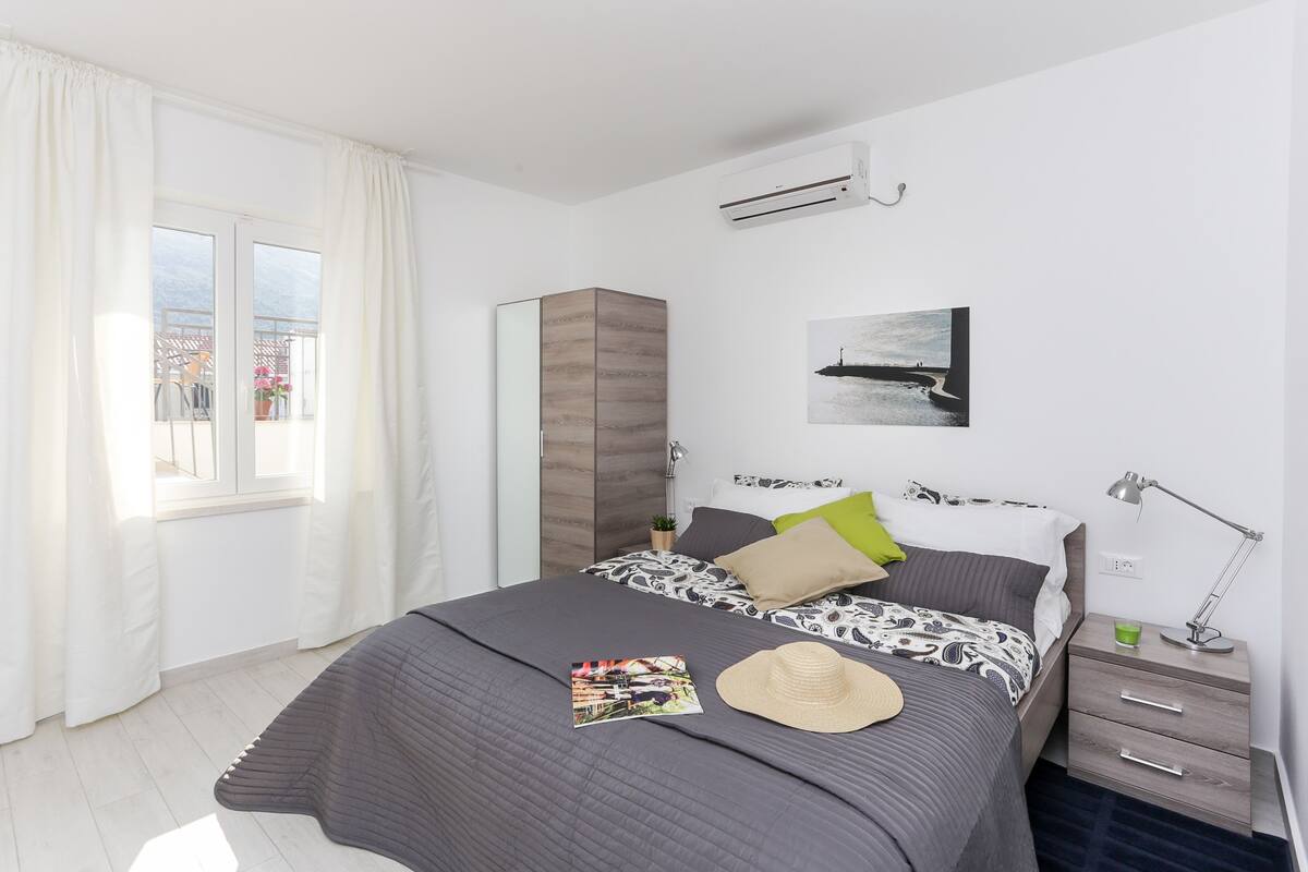 A bedroom with a bed, bedside table, lamp, and a window with curtains.