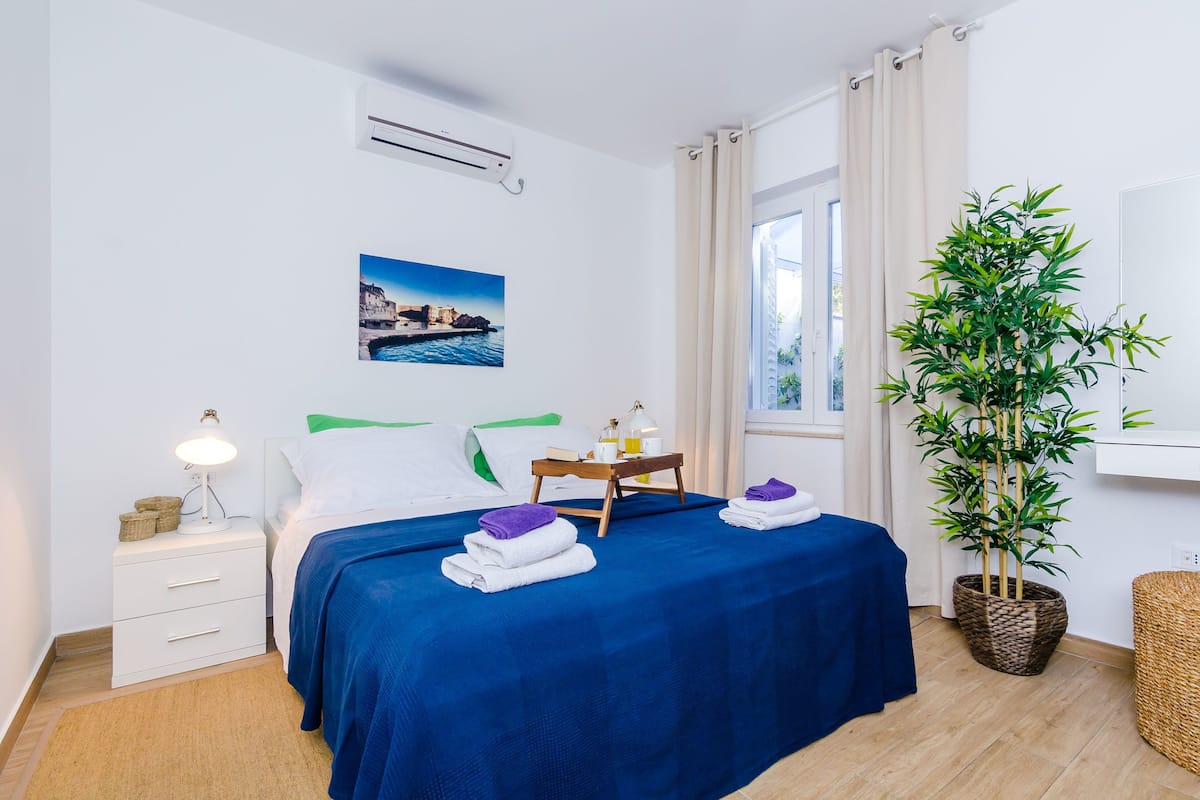 A hotel room with a bed, bedside table, lamp, and a potted plant.