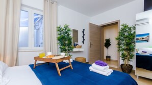 A hotel room with a bed, a breakfast tray, two potted plants, a mirror, and a view of the sea through the window. - Villa Providenca (Dubrovnik)