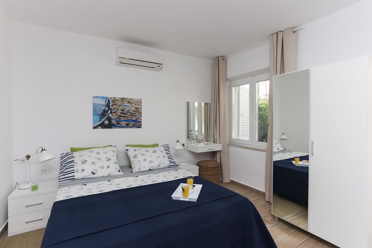 A bedroom with a bed, bedside table, lamp, and a mirror.