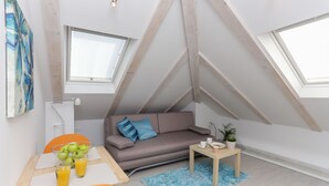 A modern loft bedroom with a sloped ceiling, a sofa, a dining table with fruit and drinks, and a small side table with a plant. - Villa Providenca (Dubrovnik)