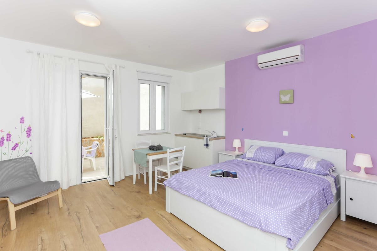 Quarto com cama, escrivaninha, cadeira, janela e ar condicionado.