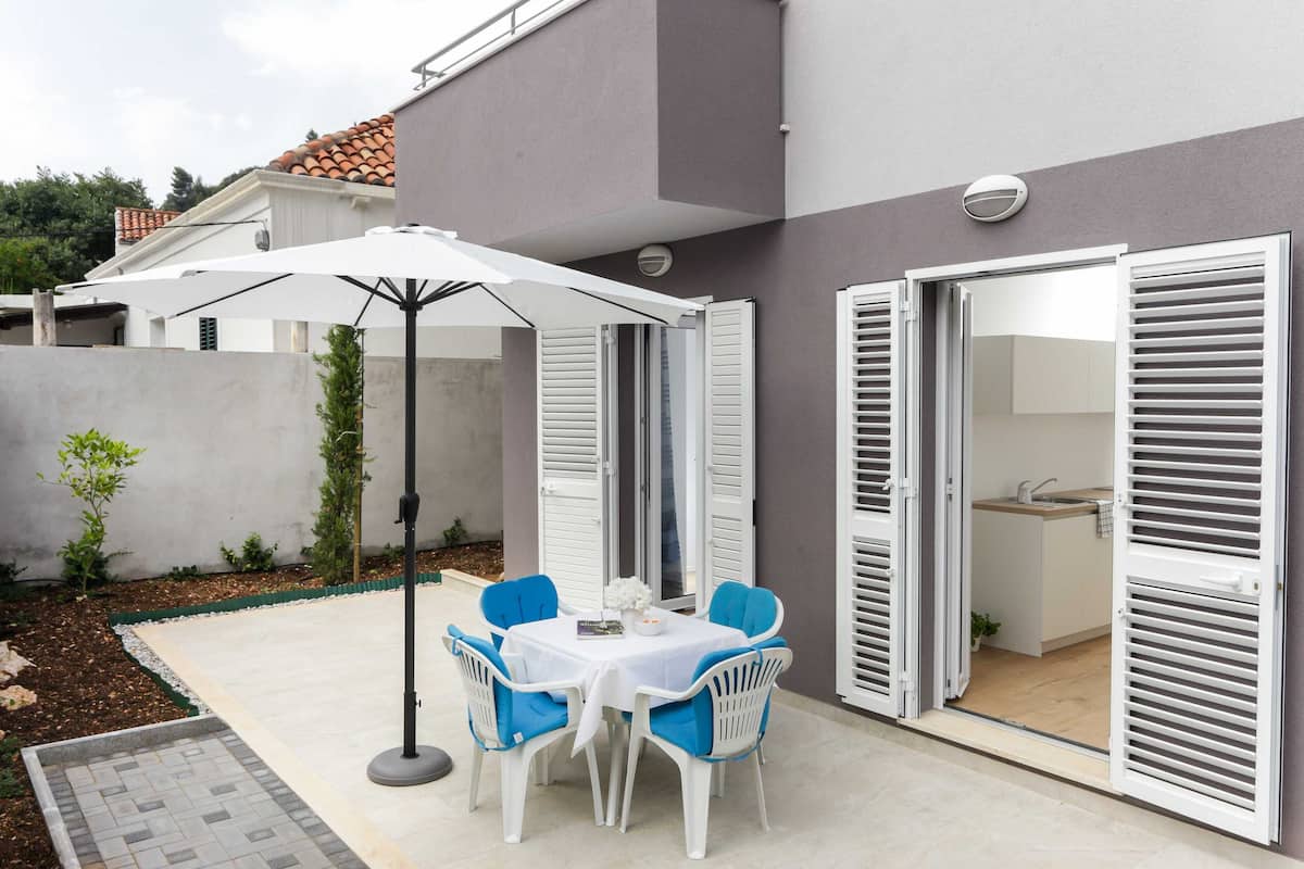 Um pátio com mesa, cadeiras, um guarda-sol e uma porta corrediça que dá para uma cozinha.