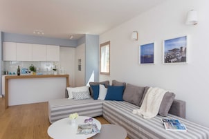 A modern living room with a grey and white striped sofa, a round coffee table with magazines, and a kitchen area in the background.