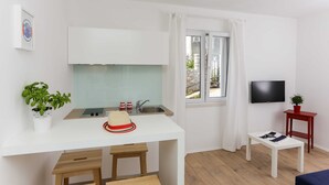 A compact kitchen with a white countertop, a sink, and a window with curtains. - Apartments Villa Karmen (Dubrovnik)
