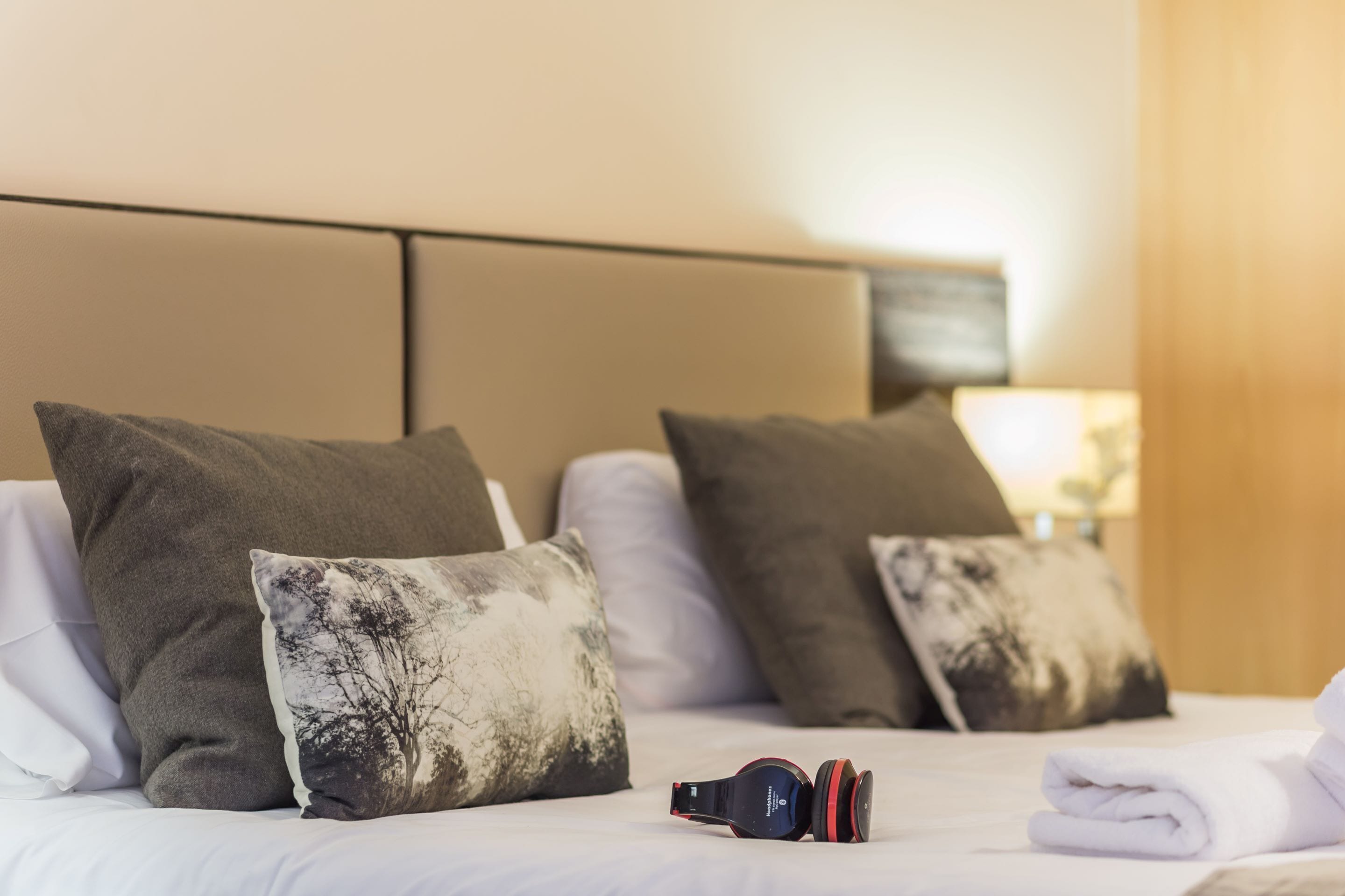 A neatly made bed with a pair of headphones on it, surrounded by pillows.