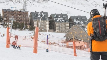 A ski slope with a person in an orange jacket and green ski boots.