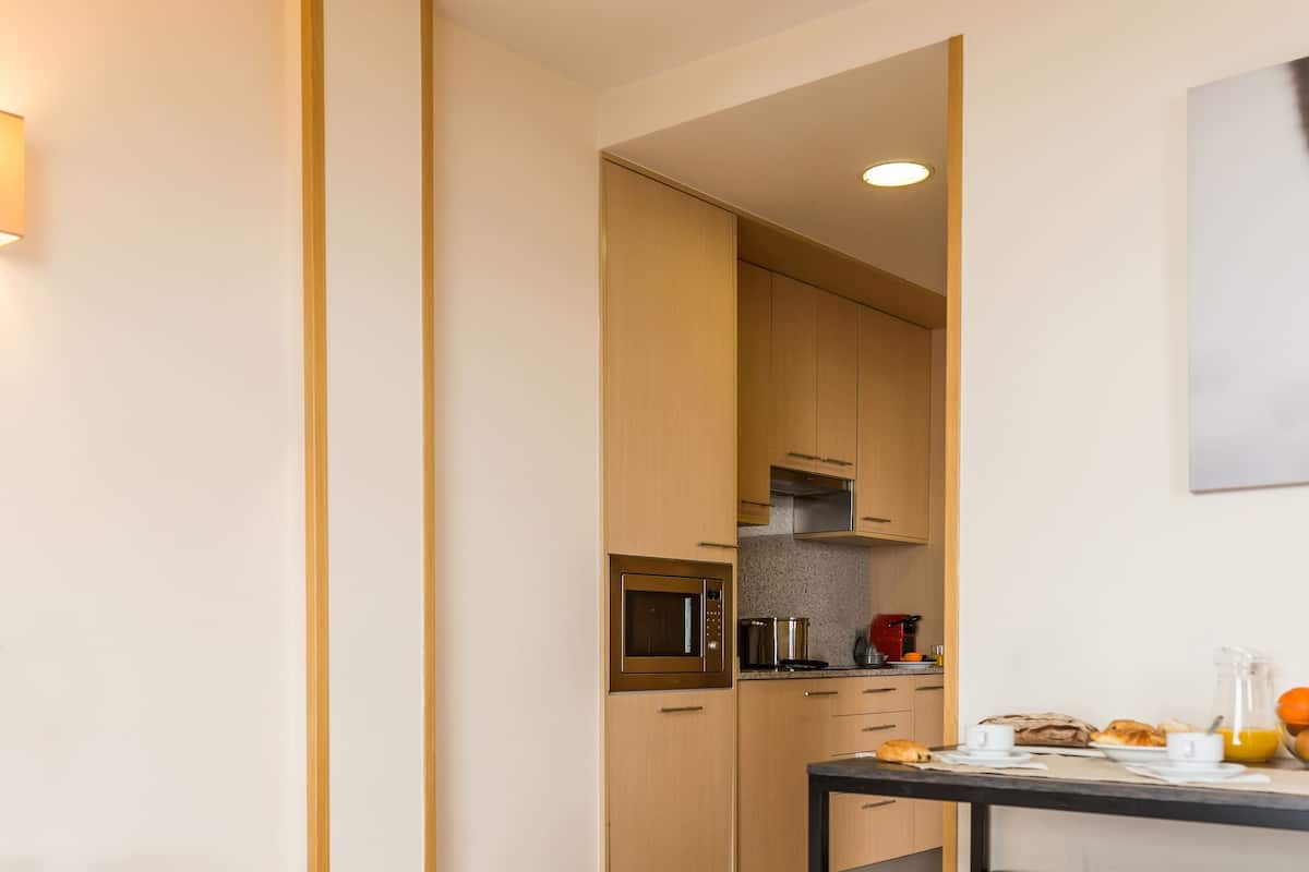 Une cuisine moderne avec des meubles en bois, une table à manger avec un banc, et des aliments pour le petit-déjeuner, comme des croissants et du jus d’orange.