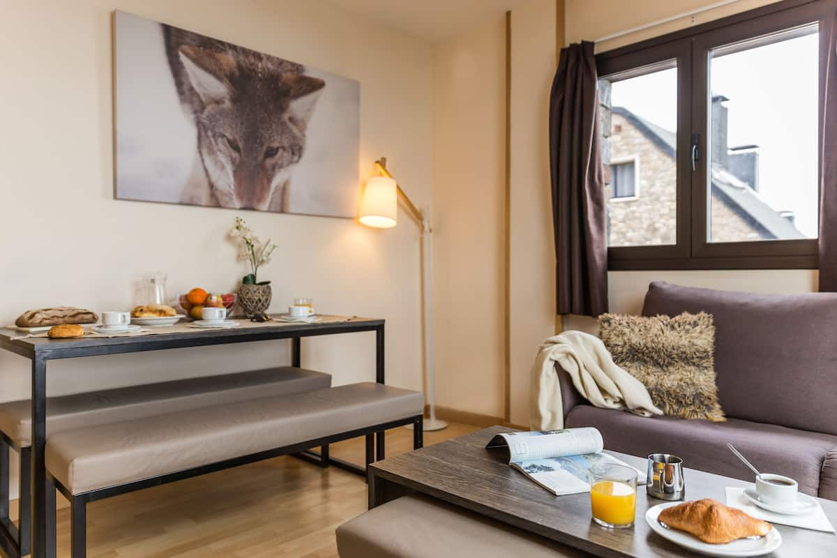Un salon moderne comprenant un canapé, une table à manger avec des aliments pour le petit-déjeuner, un banc, une lampe sur pied et une fenêtre avec des rideaux.