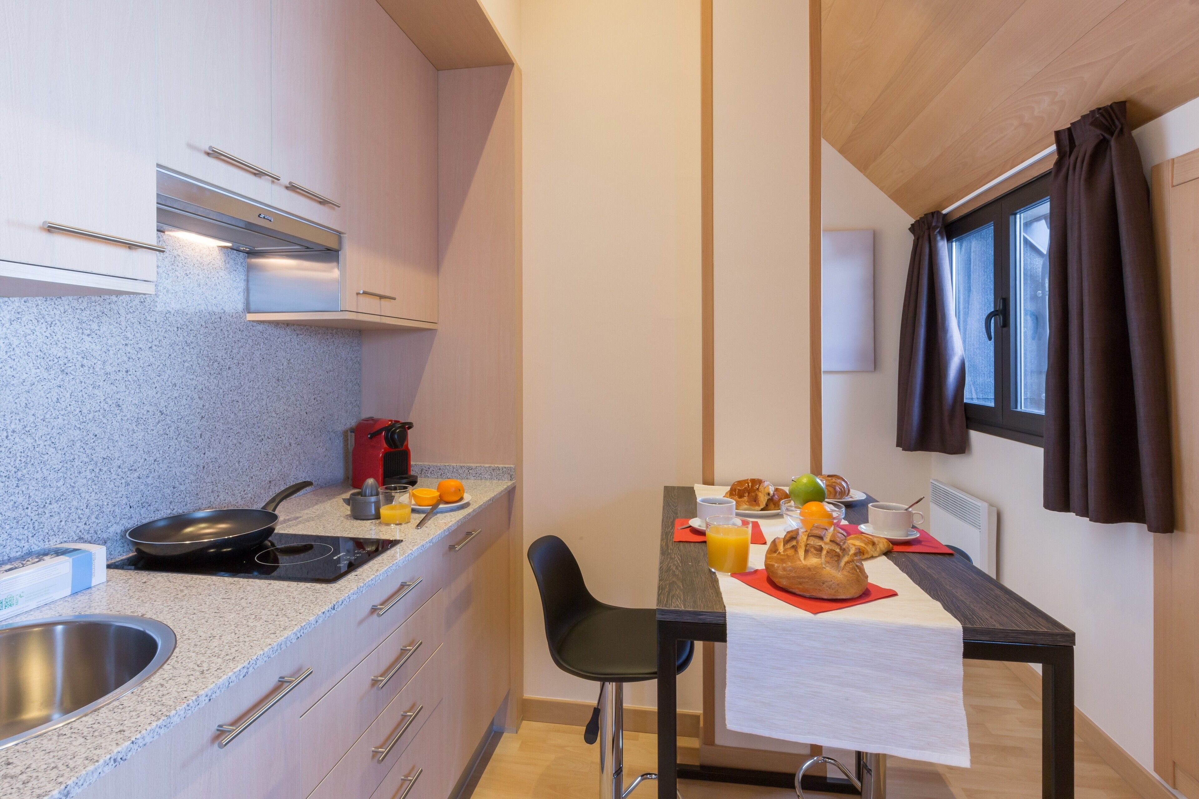 A compact kitchen with a stove, sink, and a dining area with a table set for breakfast.
