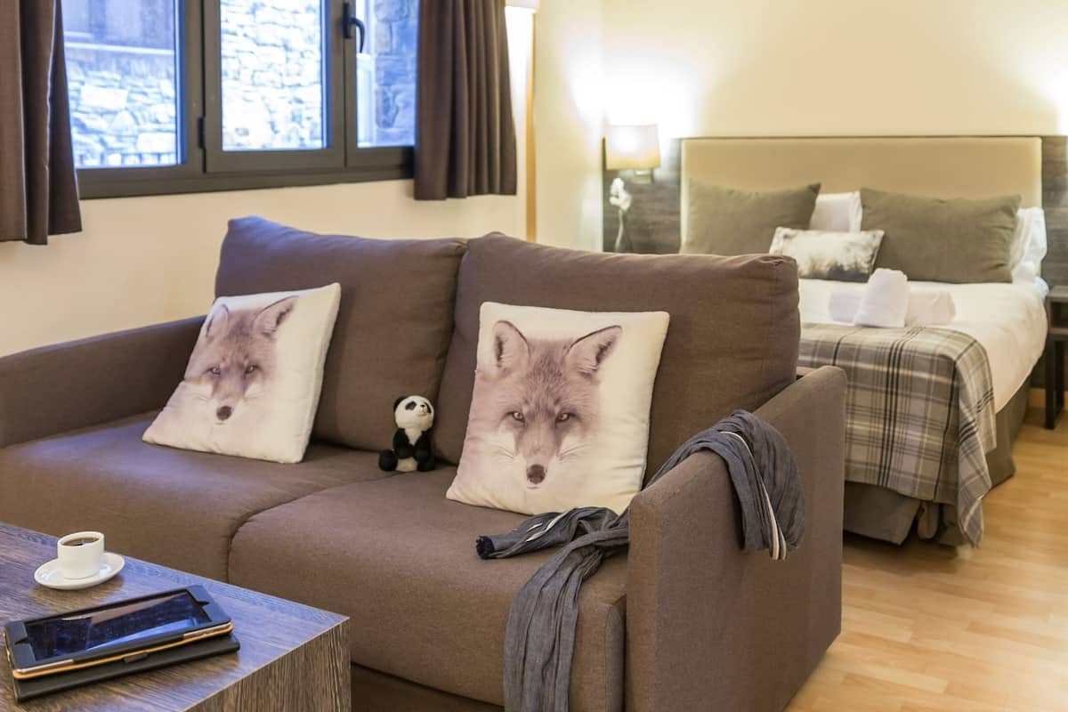 Une pièce confortable avec un canapé, un lit et une petite table sur laquelle se trouvent une tasse et une tablette.