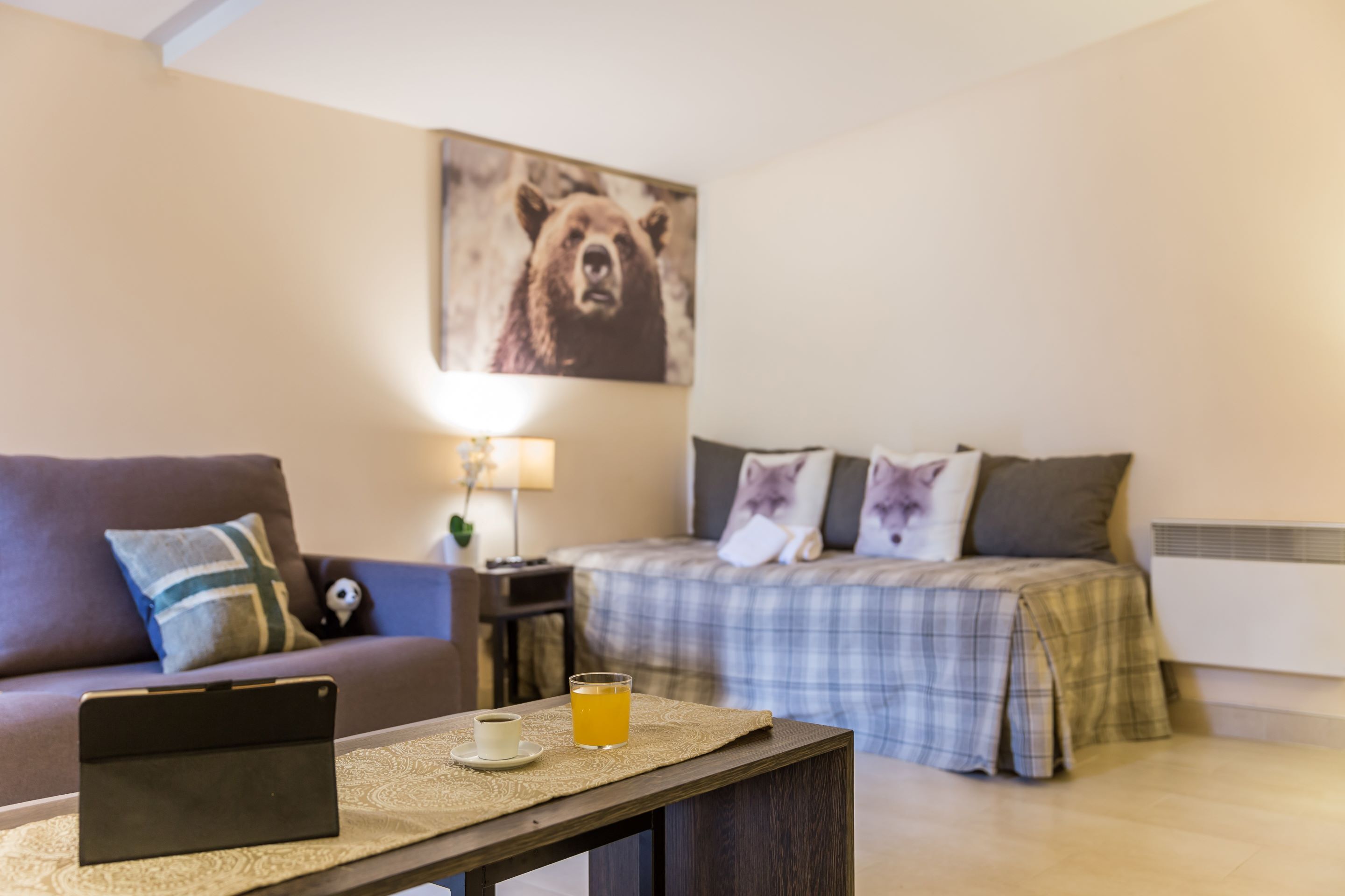 A cozy room with a bed, a sofa, a bedside table with a lamp, and a tablet on the table.
