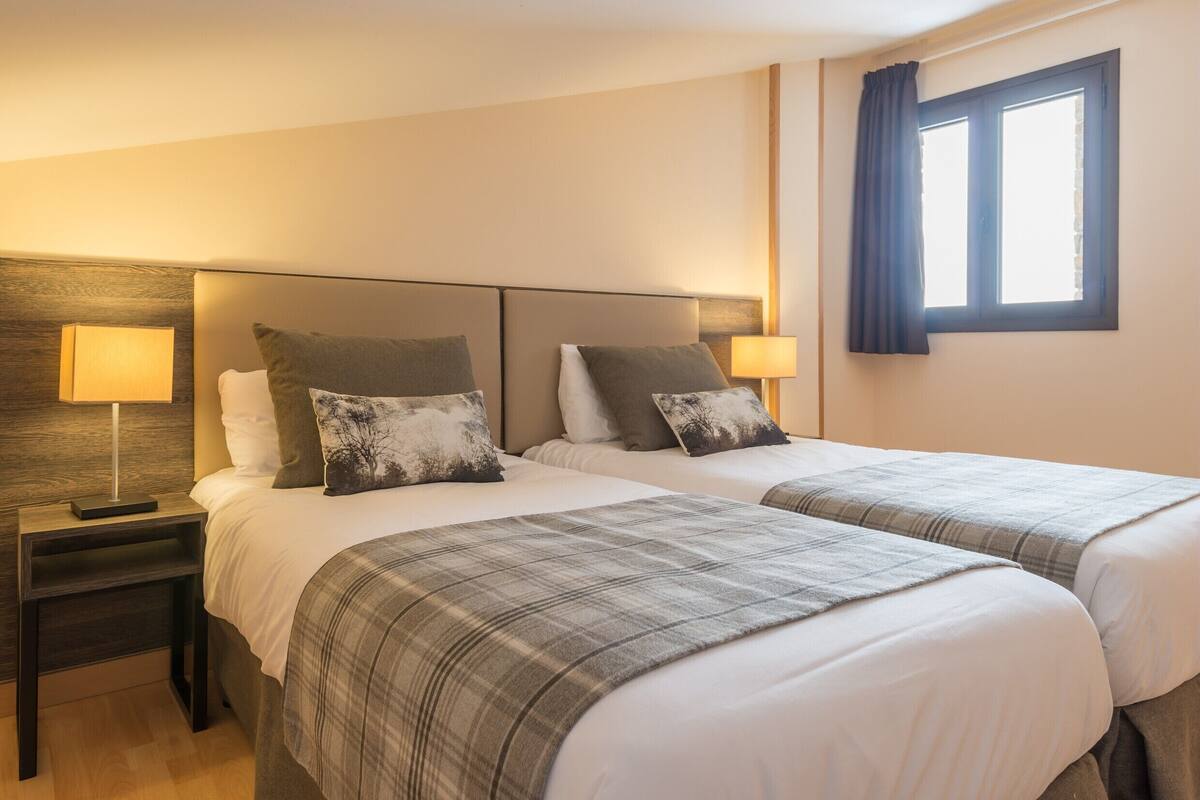 Une chambre d’hôtel avec deux lits, des tables de chevet, des lampes et une fenêtre avec des rideaux.