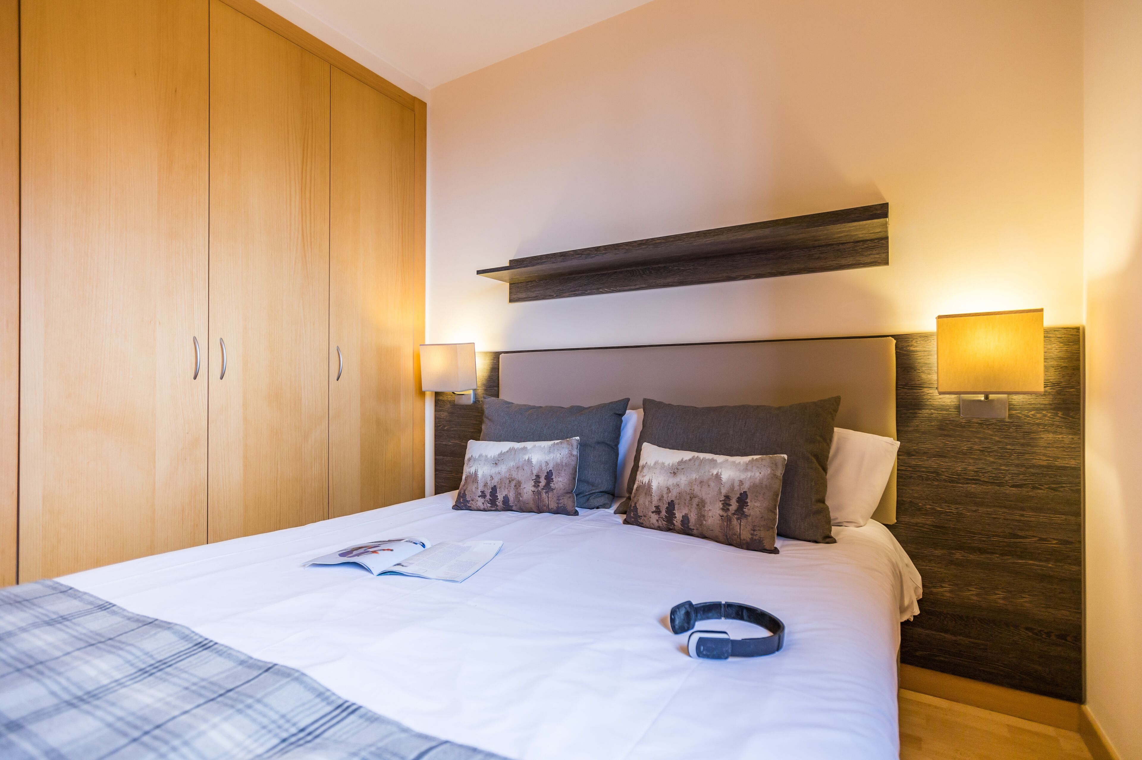Una habitación de hotel con una cama grande, un armario de madera y dos lámparas fijadas a la pared.