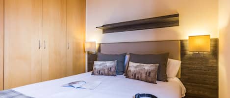 A hotel room with a large bed, wooden wardrobe, and two wall-mounted lamps.