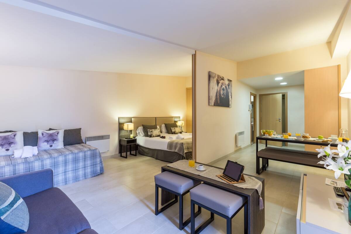 Une chambre d’hôtel moderne équipée d’un lit, d’un canapé, d’un bureau avec un ordinateur portable et d’un coin repas avec une table et des chaises.