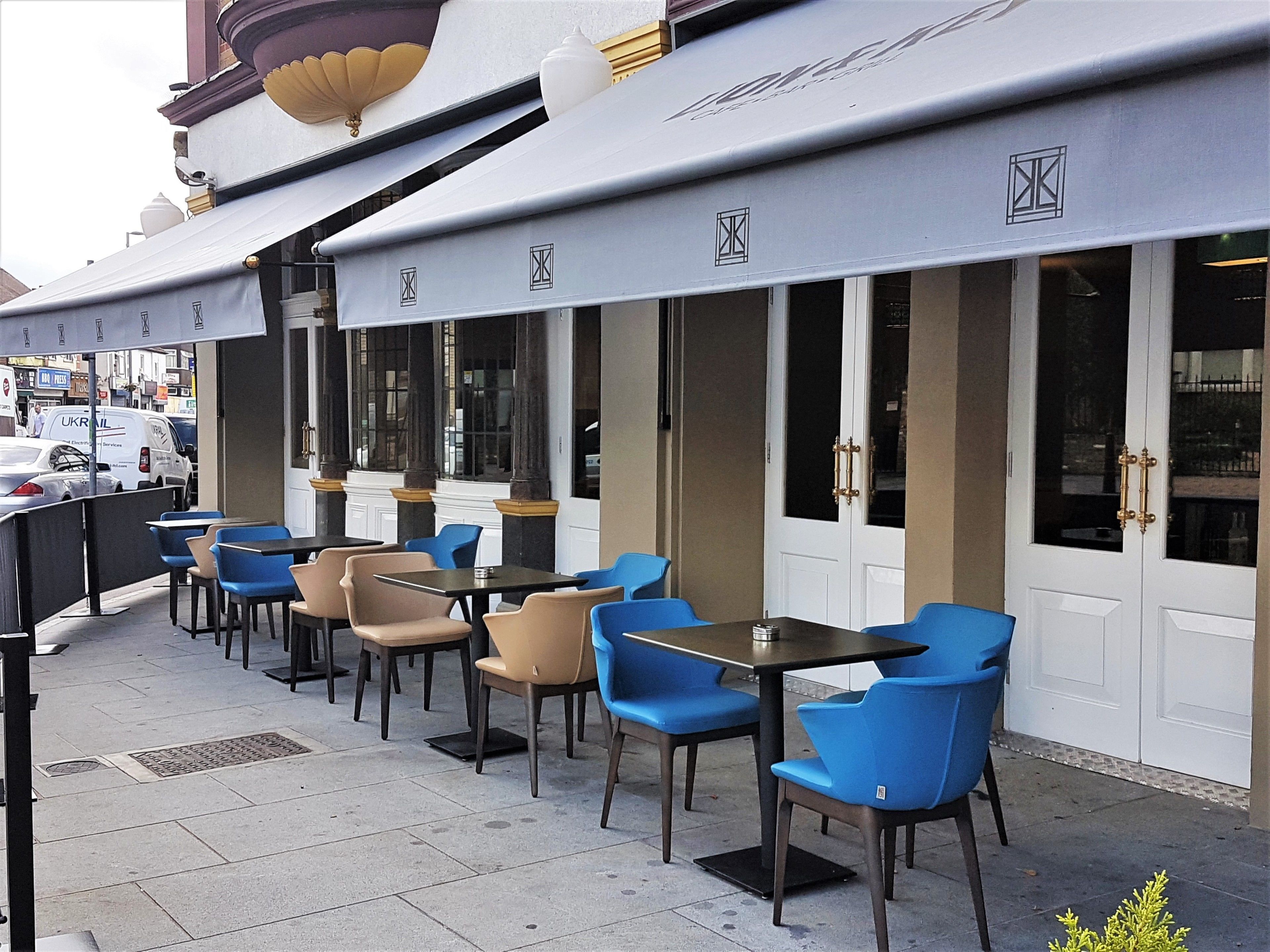 An outdoor cafe with tables and chairs, a white awning, and a door with glass panels.