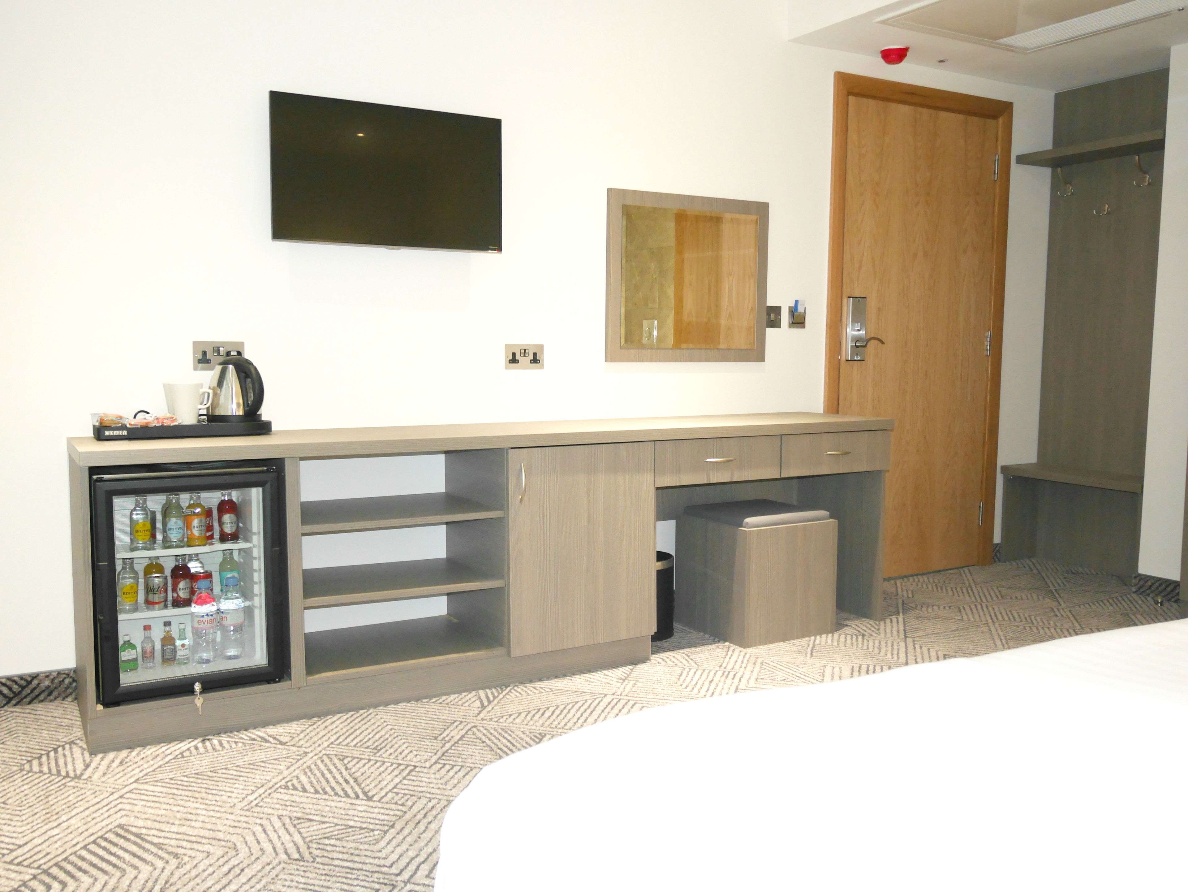 Una habitación de hotel con minibar, televisión, espejo y puerta de madera.